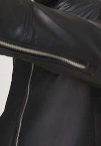 Black leather jacket featuring a zipper closure, textured finish, and distinct shoulder stitching. Includes a visible zipper accent on the sleeve.
