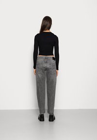 Šedé džíny s volnějším střihem, pětikapsovým designem a kontrastním šitím. Kombinovány s černým žebrovaným krátkým topem s dlouhými rukávy.