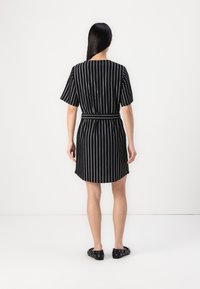 Vestido curto às riscas preto e branco com mangas curtas, um cinto na cintura e um hem em curva. Usado com sapatos pretos com acentos circulares.