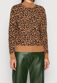 Hnědý svetr s leopardím vzorem, vysokým límcem, žebrovanými manžetami a lemem. Kombinovaný se zelenými koženými kalhotami. Měkká pletená textura.