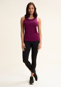 Haut de sport sans manches mauve avec un col rond, associé à un legging noir et des chaussures de sport noires. Présente une marque sur le haut et le legging.