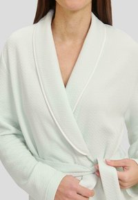 Bata de baño verde menta claro con un patrón de espiga, envuelta y atada a la cintura con ribete blanco en el cuello y las mangas.