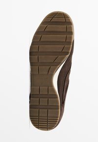 Chaussure en daim marron avec une semelle en caoutchouc présentant un motif antidérapant texturé. La semelle intérieure est accentuée de blanc avec un logo sur le côté.