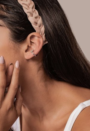 Silberne Creole mit einem kleinen Zirkonia-Akzent, die am oberen Ohr getragen wird. Langes, glattes, dunkles Haar bedeckt teilweise das Ohr.