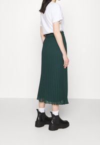 Grön veckad midikjol i lätt tyg, kombinerad med en vit t-shirt och svarta ankelboots med tjocka sulor och vita strumpor.