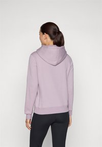 Un hoodie léger en lavande, avec une grande capuche douce, des poignets côtelés et une coupe décontractée, associé à des leggings noirs.