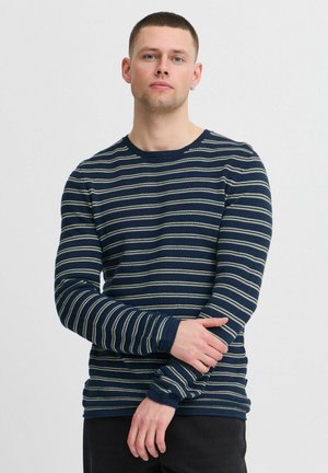 Chemise à manches longues bleu marine avec des rayures verticales crème. Fabriquée en tissu lisse, présente un col rond et une coupe ajustée.