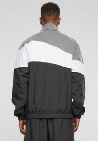 Black and white windbreaker jacket featuring a patterned mesh upper, elastic cuffs, and a waistband. Smooth texture with a relaxed fit.