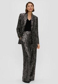 Paillettenverziertes schwarzes Anzug mit einem taillierten Sakko und weitem Hosenbein, das ein tiefes V-Ausschnitt-Oberteil, eine glatte Textur und eine glänzende Oberfläche aufweist.