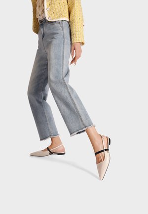 Scarpe slingback a punta in pelle beige chiaro. Presentano una fascetta nera sulla parte superiore del piede e un tacco basso e piatto. Abbinato a jeans cropped.