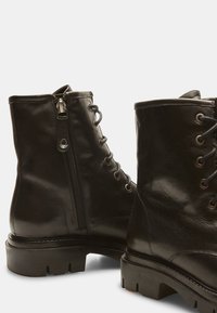 Stivali ankle in pelle nera con lacci sulla parte anteriore e cerniera laterale, dotati di una suola spessa e finitura testurizzata.