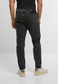 Jeans in denim nero con una vestibilità slim, dotati di due tasche posteriori a toppa e una cintura testurizzata. Indossati con sneakers bianche e beige.