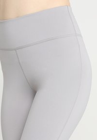 Leggings gris clair taille haute en tissu extensible, avec coutures plates et texture lisse pour le confort et l'ajustement.