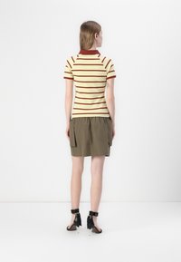 Stripet polo i gul og brun, kombinert med en khaki skirt med sidelommer. Outfitet inkluderer svarte hæler med ankelstropper og sløyfer.