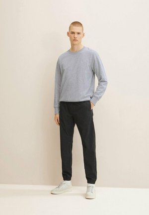 Sudadera de manga larga gris claro, pantalones jogger negros y zapatillas blancas. Diseño simple con puños y cintura acanalados, textura suave.