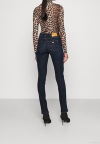 Smala mörkblå jeans med kontrastsömmar, två bakfickor och en läderlapp. Långärmad topp med leopardmönster och svarta klackstövlar.