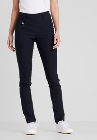 Pantalons bleu marine en matière extensible, avec une coupe slim, des poches avant et un accent en métal à la taille. Associés à des baskets blanches.