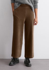 Braune Cordweite-Hosen mit glatter Textur, elastischem Bund und Seitentaschen, kombiniert mit schwarzen Schnür-Plateauschuhen.