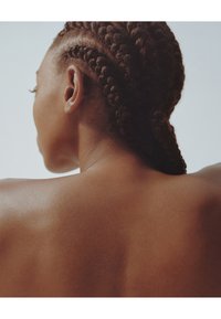 Gros plan sur le haut du dos d'une personne aux cheveux noirs tressés. Texture de peau lisse, fond neutre, mettant en valeur les contours du dos et les tresses.