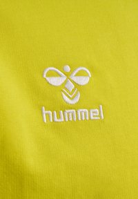Geel katoenstof met een gladde textuur, voorzien van een reliëf wit logo van "hummel" en een gestileerd bijontwerp.