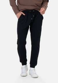 Zwarte joggingsbroek met een relaxed fit, voorzien van een elastische tailleband, een trekkoord en zijzakken. Gepaard met witte sneakers.