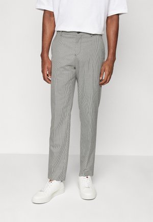 Pantalons gris à carreaux avec une coupe ajustée, dotés d'un devant plat, de poches latérales et d'une texture lisse, associés à des baskets blanches.