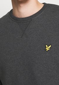 Felpa grigia realizzata in tessuto morbido, con colletto rotondo e logo di un uccello giallo ricamato sul lato sinistro. Design semplice.
