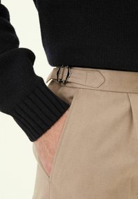 Marinblå stickad tröja med ribbade ärmslut i kombination med beige byxor. Byxorna har medföljande bälte i midjan och en sidficka.