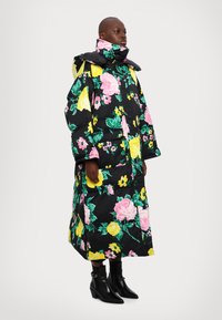 Abrigo negro acolchado con vibrantes patrones florales en rosa, amarillo y verde, cuello alto y mangas largas. Combinado con botas negras hasta el tobillo.