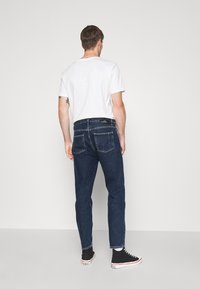 Jeans de mezclilla azul oscuro con corte recto; combinados con una camiseta blanca y zapatillas negras. Diseño minimalista con bolsillos traseros visibles.