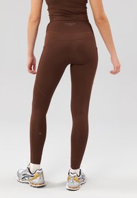 Leggings activas de tiro alto de color marrón con una textura suave y un diseño ajustado, combinados con zapatillas deportivas plateadas y doradas con cordones.