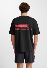 Svart t-shirt med kort ärm och röd text på ryggen, med märket "hummel" och logotyp, tillverkad av mjukt tyg.