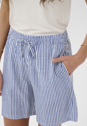 Femme portant un short à rayures verticales bleu et blanc avec une taille élastique et un cordon de serrage, main dans la poche, associé à un haut blanc.