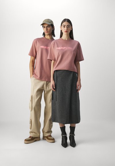 Pink short-sleeve t-shirts with "HELMUT LANG" logo, paired with beige cargo pants and a long grey skirt, worn with black ankle boots.