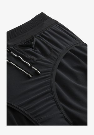 Shorts de sport noirs en tissu lisse, dotés d'une taille texturée, d'un cordon de serrage et de détails de plis subtils.