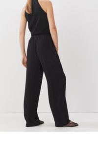 Czarne spodnie z szerokimi nogawkami, elastycznym pasem, miękkiego materiału i dwoma kieszeniami; w zestawie z czarnymi płaskimi butami z siateczki.