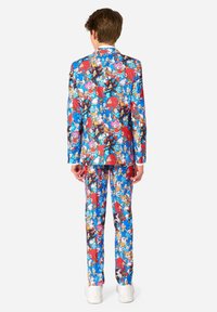 Costume coloré avec un imprimé de personnages de dessin animé éclatant en bleu, rouge et noir, accompagné de pantalons assortis et de chaussures blanches.