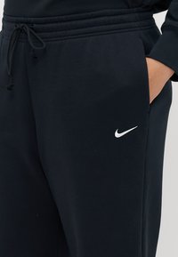 Tamno plave Nike trenirke od mekanog, teksturiranog pamuka. Imaju elastičnu traku u struku s podesivim vezicama i bijeli logotip kao akcent.