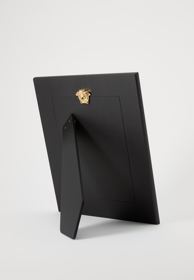 Melnas fotogrāfiju rāmītis ar statīvu; tam ir zelta lauvas formas metāla dekors un gluda matēta virsma aizmugurē.