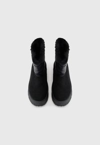 Bottines noires avec un intérieur en peluche, présentant un extérieur lisse et une semelle en caoutchouc texturée, conçues pour la chaleur et le confort.