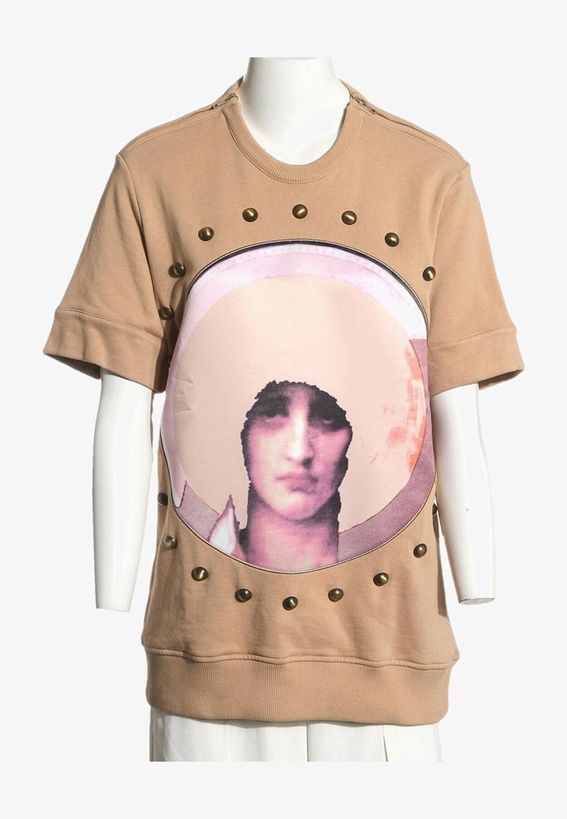 Chemise à manches courtes couleur fauve avec un grand imprimé circulaire d'un visage féminin stylisé et des clous en laiton autour du cercle.