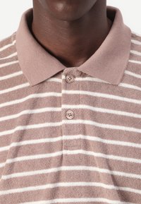 Brun og hvid stribet polo-shirt lavet af tekstureret stof, med en ribbet krave og tre-knaps lukning.