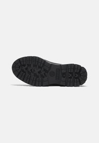 Black rubber sole with deep treads for traction. Features a logo at the center and pronounced grooves for durability and grip.