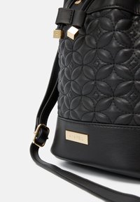 Czarna skórzana torebka z pikowanym kwiatowym wzorem, złotymi akcentami hardware i regulowanym paskiem. Posiada metalową plakietkę z nazwą marki.