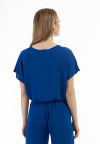 Blå jumpsuit med korte, svævende �ærmer og en afslappet pasform, der har en samlet talje og et glat, let stof.
