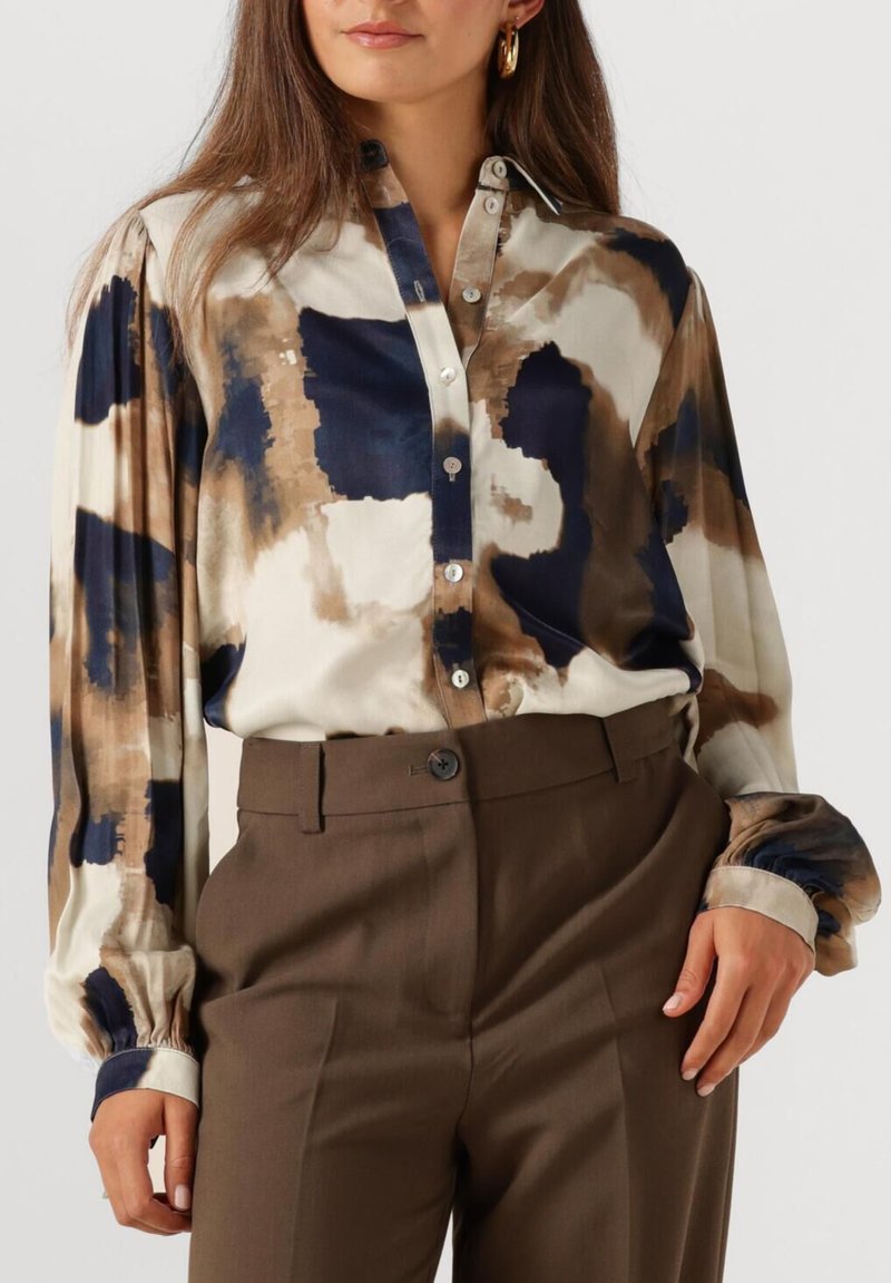 Button-up blouse featuring a beige, navy, and brown abstract pattern, long sleeves with elastic cuffs, and a classic collar. Paired with brown trousers.