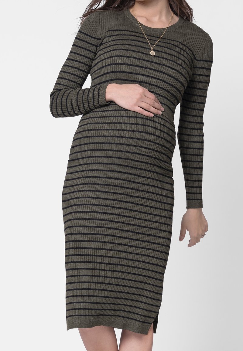 Femme enceinte portant une robe côtelée olive à manches longues avec des rayures horizontales noires, tenant son ventre d'une main.