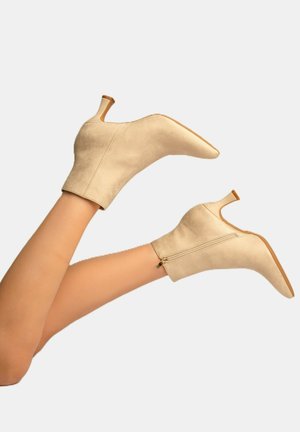 Stivaletti beige in suede, con punta affilata e tacco sottile. Presentano una cerniera laterale e una texture liscia.