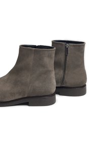 Botas de ante hasta el tobillo en gris topo con cremallera lateral, puntera redonda y suela de goma plana. Superficie texturizada con detalle de costura tonal.