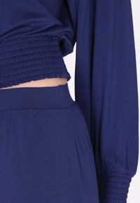 Navy-blauwe twee-delige outfit met een gesmokte crop top met lange mouwen en bijpassende hoge taille broek, beide van zachte, rekbare stof.